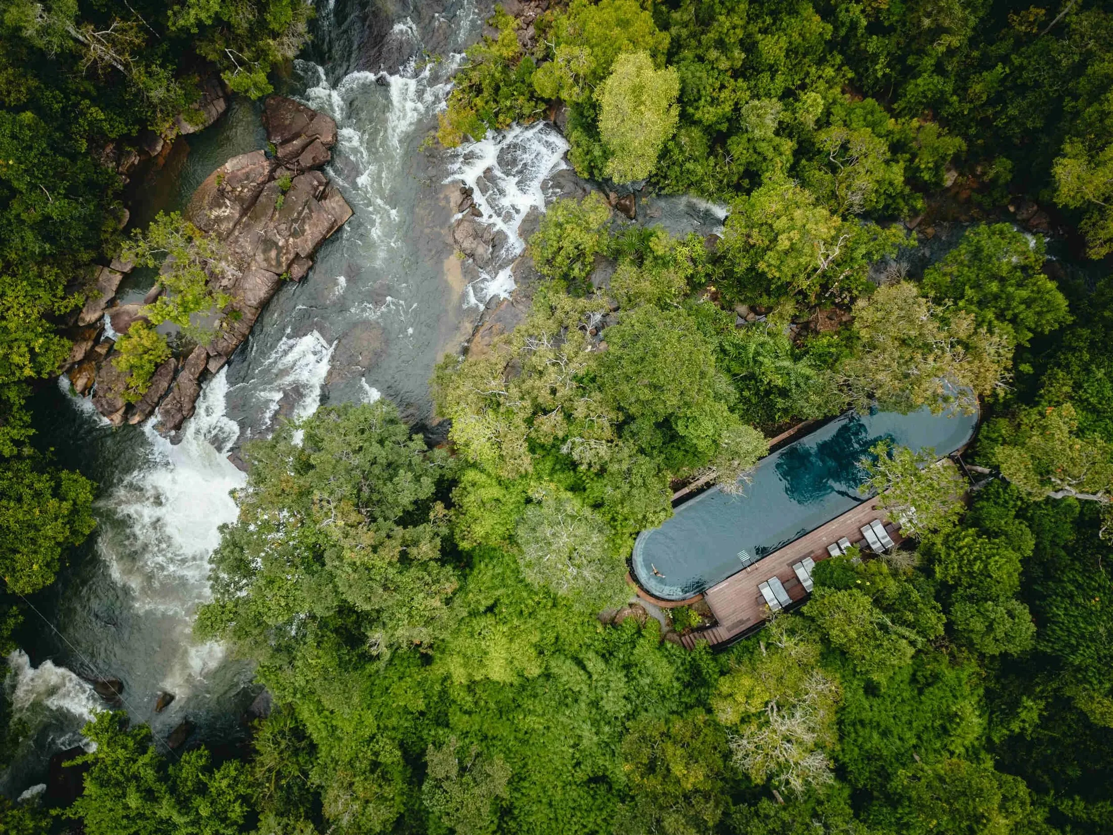 A private pool deep in the forest, seen from above beside a river and waterfalls